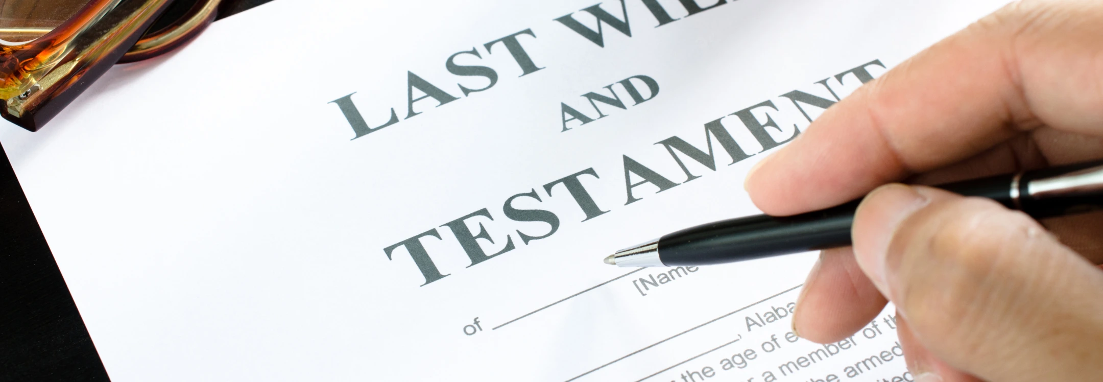 Person signing a Last Will and Testament document with a pen, symbolizing estate planning and legal documentation.