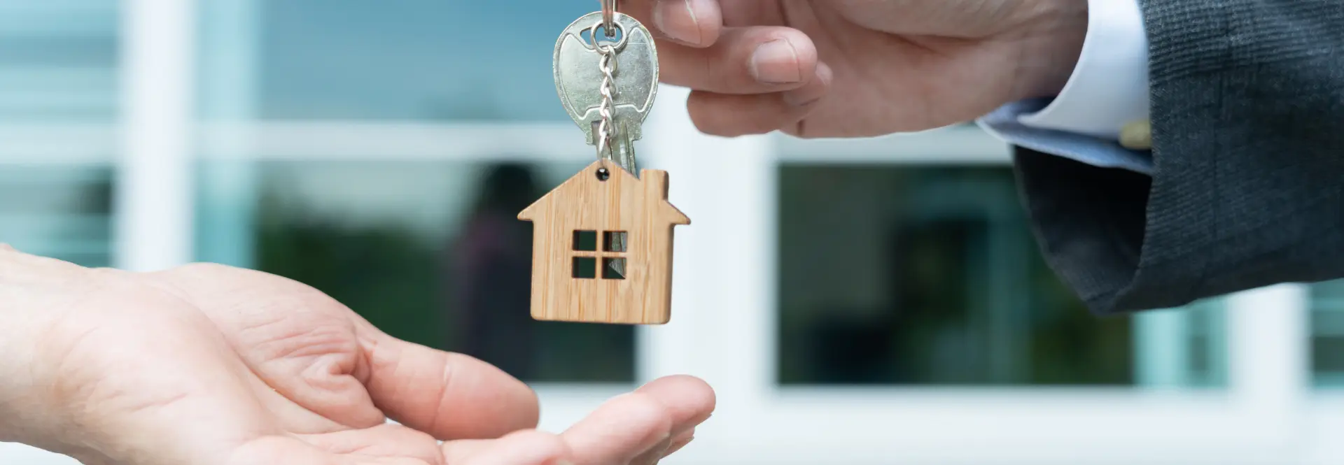A person handing over a house-shaped keychain to another person's open hand, symbolizing a property handover as part of a rental lease agreement.